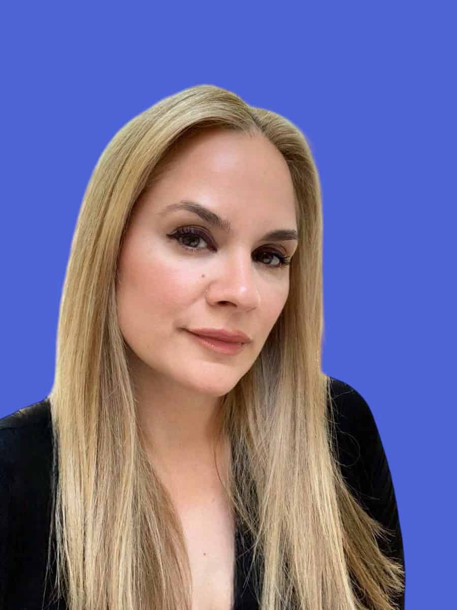 Sophisticated woman with blonde hair and elegant makeup, professional portrait against a vibrant blue background, representing business, confidence, and modern corporate aesthetics.