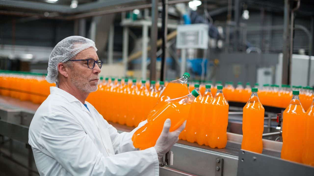 Vega Global Group orange soda production in a modern beverage manufacturing facility. Quality control and packaging process for soft drinks in an industrial setting.