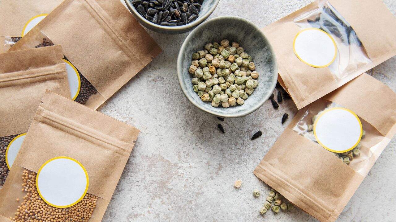 Assorted organic spices and herbs in kraft paper packaging with labeled circular stickers, on a light textured surface, emphasizing natural ingredients and sustainable packaging for health and wellness.